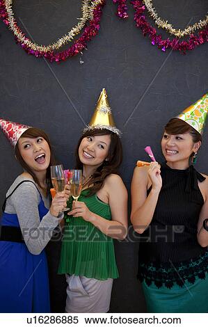 Three young women wearing party hats and holding glasses of champagne, black background View Large Photo Image Stock Photography - Three young women wearing party hats and holding glasses of champagne, black background. Fotosearch