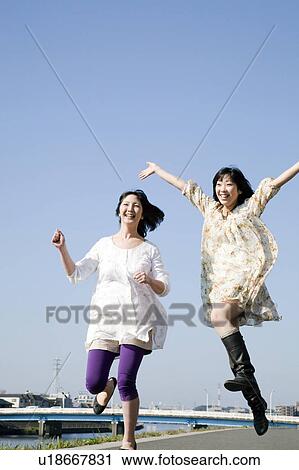 Stock Image - Tow Young Women Jumping Under Blue Sky. Fotosearch