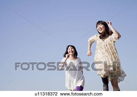 Stock Image - Tow Young Women Running Under Blue Sky. Fotosearch