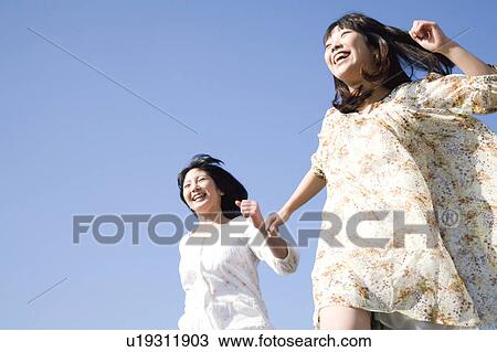Stock Image - Tow Young Women Running Under Blue Sky. Fotosearch