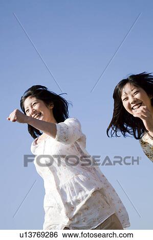 Stock Photograph - Tow Young Women Running Under Blue Sky. Fotosearch