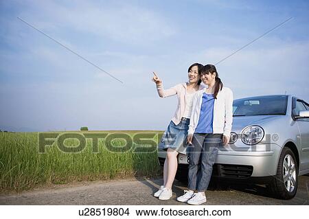Picture - Two Female Friends Leaning on Car at Countryside. Fotosearch
