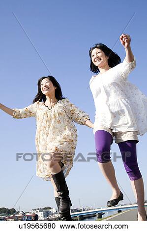 Stock Image - Two Young Women Holding Hands and Jumping. Fotosearch