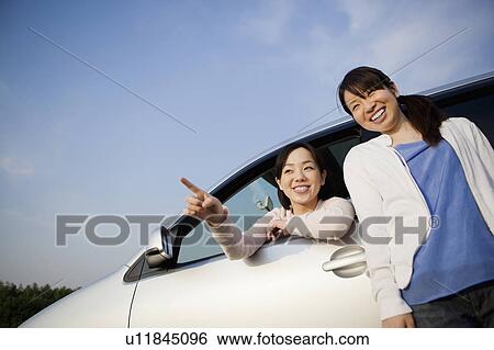 Stock Photograph - Two Young Women Looking at View by Car. Fotosearch