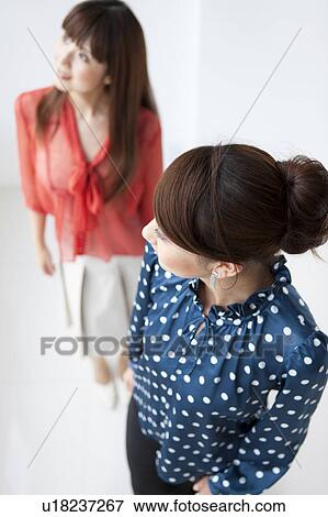 Stock Photo - Two young women smiling and looking away, white background. Fotosearch