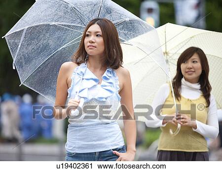 Two young women with umbrella walking down the street View Large Photo Image Stock Image - Two young women with umbrella walking down the street. Fotosearch
