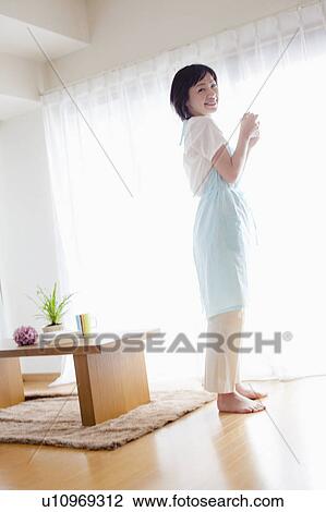 Stock Image - Woman Standing in Living Room by Window. Fotosearch