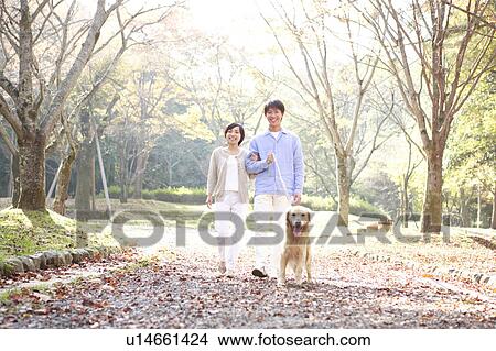 Picture - Young Couple and a Domestic Dog Talking A Walk in Park. Fotosearch