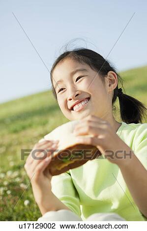 Stock Image - Young Girl Eating Sandwich Outdoors. Fotosearch