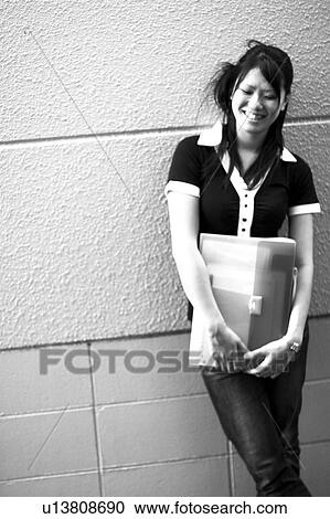 Young woman holding a file and leaning on wall View Large Photo Image Stock Image - Young woman holding a file and leaning on wall. Fotosearch