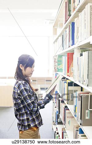 Stock Image - Young woman looking at book in library, Japan. Fotosearch