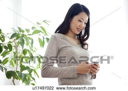 Young woman looking at mobile phone, smiling View Large Photo Image Stock Image - Young woman looking at mobile phone, smiling. Fotosearch