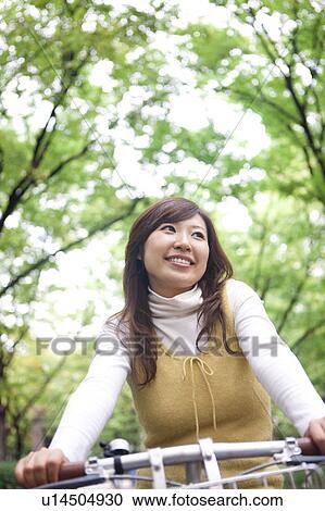 Stock Image - Young woman riding bicycle, smiling. Fotosearch