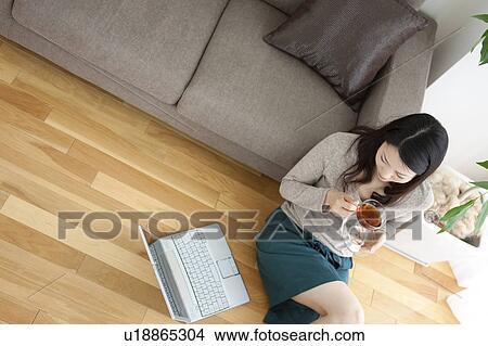 Picture - Young woman sitting of floor, looking at laptop. Fotosearch