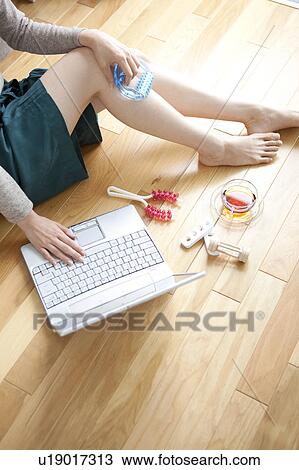 Stock Image - Young woman sitting of floor, using laptop. Fotosearch