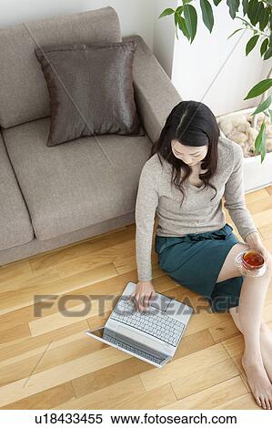 Stock Photography - Young woman sitting of floor, using laptop. Fotosearch
