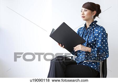 Young woman sitting on chair, holding file, white background, copy space View Large Photo Image Stock Photo - Young woman sitting on chair, holding file, white background, copy space. Fotosearch