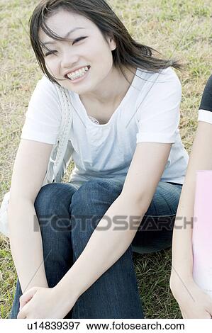 Stock Photo - Young woman sitting on grass looking at camera. Fotosearch
