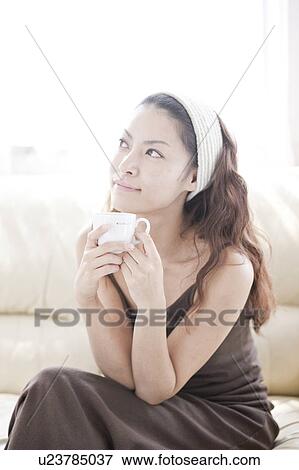 Young woman sitting on sofa, holding mug View Large Photo Image Stock Photo - Young woman sitting on sofa, holding mug. Fotosearch