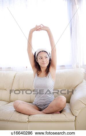 Stock Photograph - Young woman sitting on sofa, stretching. Fotosearch