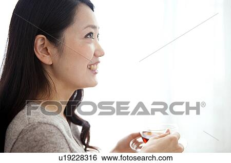Stock Photograph - Young woman smiling, holding cup of tea, copy space. Fotosearch