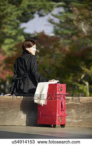 Stock Image - Young Woman With Luggage Sitting on Bench. Fotosearch