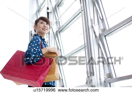 Young woman with shopping bags standing by window View Large Photo Image Stock Photograph - Young woman with shopping bags standing by window. Fotosearch