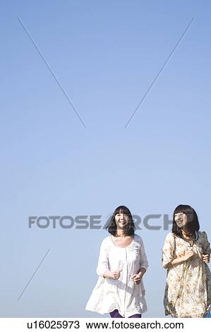 Stock Image - Young women running side by side, Japan. Fotosearch