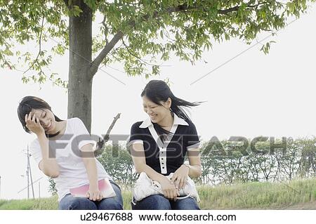 Stock Photo - Young women sitting on grass smiling. Fotosearch