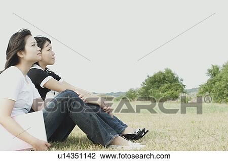 Stock Image - Young women sitting on grass. Fotosearch