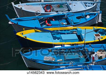Stock Image - Aerial close up view of colourful blue and yellow fishing boats moored in vivid green clear water, sunny spring afternoon, Salento, Puglia, Southern Italy. Fotosearch