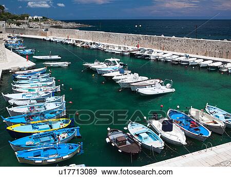 Aerial view of colourful fishing boats moored in sheltered harbour, vivid green clear water, blue sea and sky beyond, sunny spring afternoon, Salento, Puglia, Southern Italy View Large Photo Image Stock Photo - Aerial view of colourful fishing boats moored in sheltered harbour, vivid green clear water, blue sea and sky beyond, sunny spring afternoon, Salento, Puglia, Southern Italy. Fotosearch