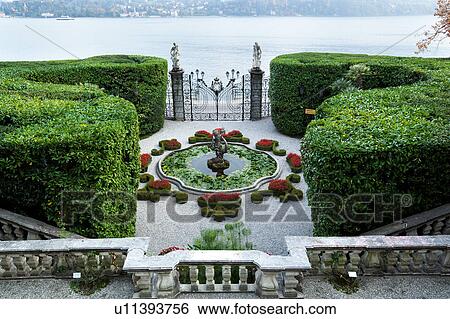 Stock Photograph - Aerial view of Villa Carlotta showing ornamental gardens, terraced stairways, fountain with statue and lake front beyond ornate wrought iron gateway, Lake Como, Northern Italy. Fotosearch