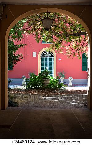 Picture - Arched entrance of Renaissance palazzo with painted pink wall on opposite side of courtyard, with statue and garden ornamentation, Bologna, Italy. Fotosearch
