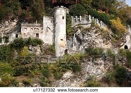 Stock Image - Castle ruins built into hillside with merloned tower and outer walls visible, surrounded by rock, bushes and ferns growing on hillside, Northern Italy. Fotosearch