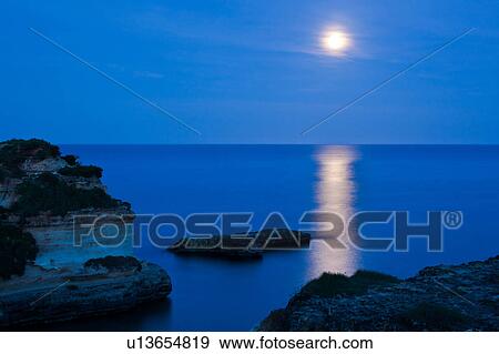 Stock Photo - Cliffs and rocky coastline of Salento at twilight, with full moon reflection on calm sea, Puglia, Southern Italy. Fotosearch