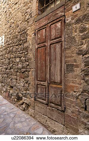 Picture - Close up of old wooden door, red peeling paint, and medieval wall of house with traditional combination of red brick and local grey stone, cobbled street.. Fotosearch
