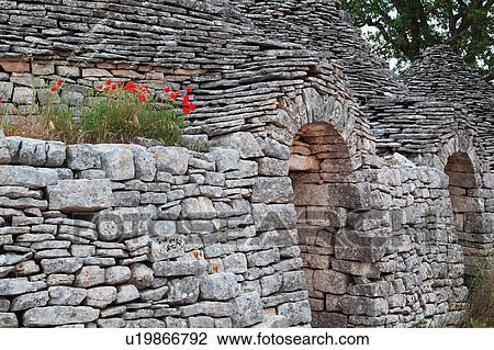 Close up view of trullo: traditional house of uncemented stones, with arched doorways and conical roof, wild poppies growing on ledge, sunny spring afternoon, Locorotondo, Puglia, Southern Italy View Large Photo Image Stock Image - Close up view of trullo: traditional house of uncemented stones, with arched doorways and conical roof, wild poppies growing on ledge, sunny spring afternoon, Locorotondo, Puglia, Southern Italy. Fotosearch