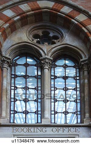 Stock Photograph - Detail of arched stone window, with 2 arches and rosette detail, ornate lead glass panels, surrounded by red and white striped brick detail, St. Pancras International railway station, London, England. Fotosearch