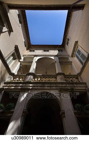 Stock Image - Detail of inner open courtyard of Italian Renaissance palazzo, with stucco walls, arched windows and balustrade, showing blue sky above, Todi, Umbria. Fotosearch