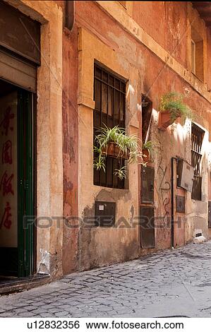 Stock Photograph - Detail of side street with orange stucco walls, hanging plants and graffiti, cobblestone paving. Fotosearch