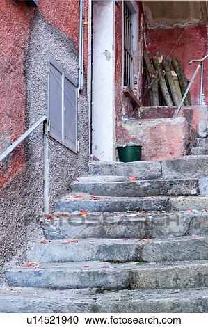 Stock Image - Detail of steep uneven stone stairway up narrow alley with walls of houses painted red/orange in typical evocative style of Northern Italy. Fotosearch