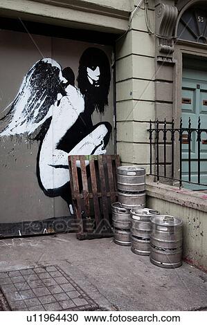 Stock Image - Early morning in Dublin, with empty metal beer kegs lined up outside doorway, with stunning black and white graffiti angel painted on door, Dublin, Southern Ireland. Fotosearch