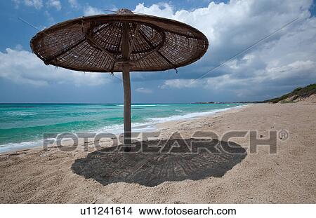 Empty, fine sandy beach, with single wicker beach umbrella casting shadow; white foam, green sea colour, blue sunny sky, with storm threatened, Salento, Puglia, Southern Italy View Large Photo Image Picture - Empty, fine sandy beach, with single wicker beach umbrella casting shadow; white foam, green sea colour, blue sunny sky, with storm threatened, Salento, Puglia, Southern Italy. Fotosearch