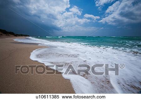 Empty, fine sandy beach with white foam of rough sea, green sea colour, blue sunny sky, with storm threatened, Salento, Puglia, Southern Italy View Large Photo Image Stock Photography - Empty, fine sandy beach with white foam of rough sea, green sea colour, blue sunny sky, with storm threatened, Salento, Puglia, Southern Italy. Fotosearch