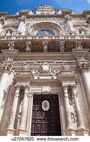 Stock Image - Facade of church of Santa Croce, exuberant Baroque ornamentation of facade with rose window, as seen from below, sunny spring morning with blue sky, Lecce, Salento, Puglia, Southern Italy. Fotosearch