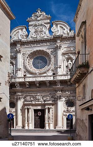 Stock Image - Facade of church of Santa Croce, exuberant Baroque ornamentation of facade with rose window, with street and steps to doorway, sunny spring morning with blue sky, Lecce, Salento, Puglia, Southern Italy. Fotosearch
