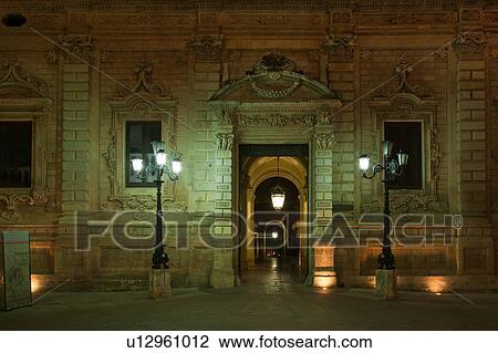 Facade of palazzo adjoining church of Santa Croce, exuberant Baroque ornamentation of facade with wrought iron lamps, entrance to courtyard and loggia, dusk with night illumination, Lecce, Salento, Puglia, Southern Italy View Large Photo Image Stock Image - Facade of palazzo adjoining church of Santa Croce, exuberant Baroque ornamentation of facade with wrought iron lamps, entrance to courtyard and loggia, dusk with night illumination, Lecce, Salento, Puglia, Southern Italy. Fotosearch