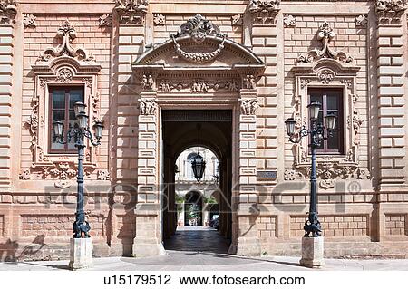 Stock Image - Facade of palazzo adjoining church of Santa Croce, exuberant Baroque ornamentation of facade with wrought iron lamps, entrance to courtyard and loggia, sunny spring morning, Lecce, Salento, Puglia, Southern Italy. Fotosearch