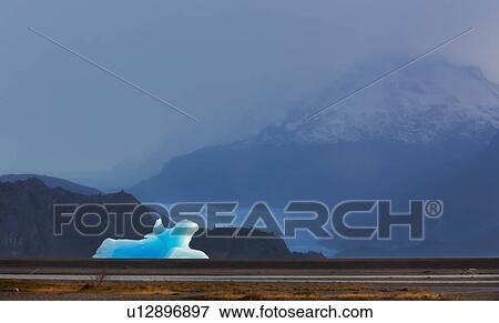 Stock Photo - Floating blue iceberg in front of Lago Grey glacier, with snowcapped mountains beyond, on misty autumn day, Torres del Paine, Southerm Chile, Patagonia. Fotosearch